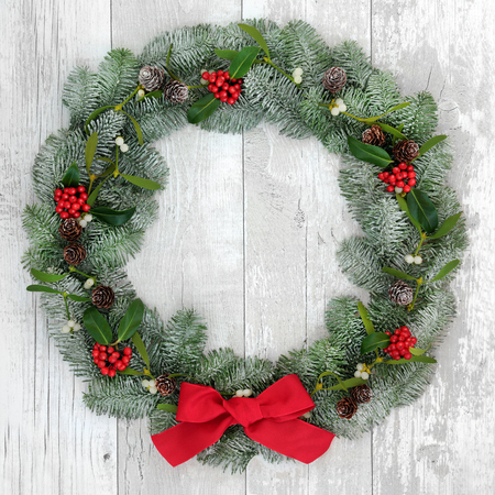 Traditional christmas wreath decoration with holly, fir and mistletoe over distressed white wood front door background.の写真素材