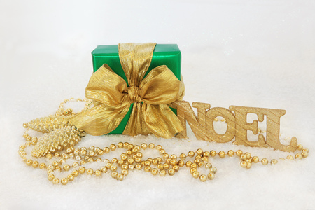 Christmas gift box with gold bow, glitter noel sign, pine cone baubles and bead decorations on snow...