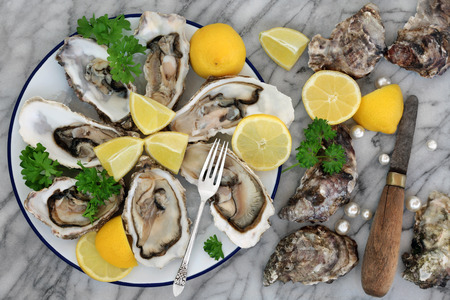 Oysters on crushed ice with antique oyster knife and silver fork with lemon fruit and pearls on a...
