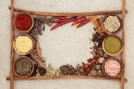 Spice and herb seasoning with cinnamon sticks forming an abstract border on natural hemp paper background.の写真素材