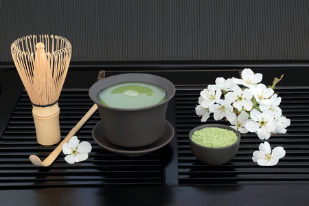 Japanese green matcha tea with cup, whisk, scoop, powder and cherry blossom on black tray background. Health drink concept.の写真素材