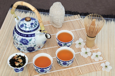 Jasmine tea with cherry blossom, stone buddha head, teapot, cups, leaves and whisk on bamboo.  Also...