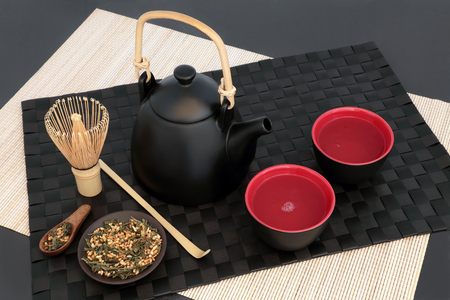 Japanese genmaicha fujiyama tea with oriental teapot, cups, whisk,scoop and dried leaves on black mat, bamboo and slate background. Has many health benefits.の写真素材