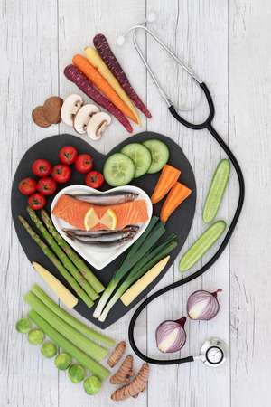 Health heart food for fitness concept with fresh fish and vegetables on heart shaped slate board on rustic background with stethoscope. High in omega 3 fatty acids, antioxidants, anthocyanins, minerals, vitamins and dietary fiber. Top view.の写真素材