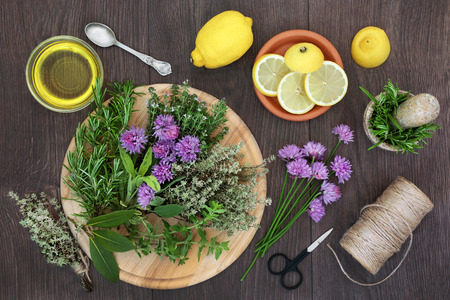 Herb seasoning with fresh herbs also in flower with lemon fruit and olive oil, with string and scissors to hang and dry leaves. On rustic oak wood background, top view.の写真素材