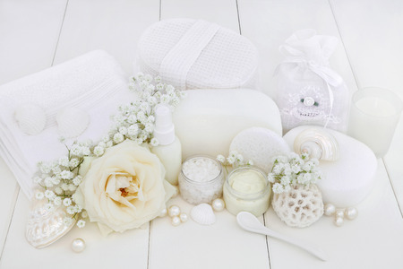 Bridal spa and beauty treatment products with rose and gypsophila flowers, ex foliating salt, moisturising cream, body lotion, sponges, wash cloths, shells and decorative pearls on white wood background.の写真素材