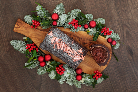 Christmas chocolate log yule cake with traditional winter flora of snow covered fir, holly and mistletoe on rustic wooden board and oak table background.の写真素材