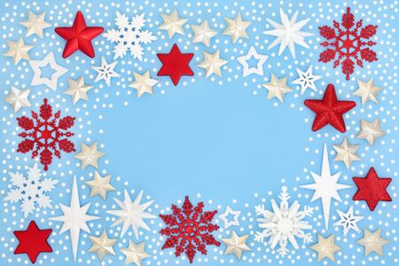 Christmas background border with star and snowflake bauble decorations with tiny snowflakes on pastel blue background with copy space.の写真素材