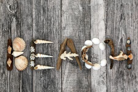 Abstract of driftwood, seashells and pebbles forming the word beach on rustic wood background.の写真素材