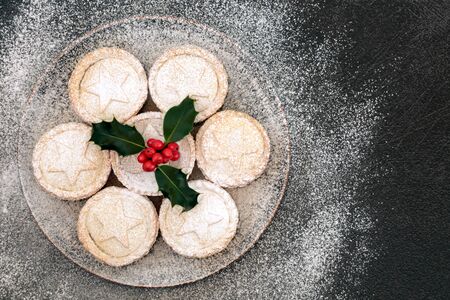 Homemade Christmas mince pies on a plate with winter berry holly and icing sugar dusting on grey grungeの写真素材