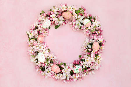 Easter wreath with spring apple blossom flowers & decorated eggs on mottled pink background.の写真素材