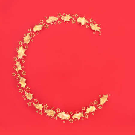 Abstract Christmas concept design with a capital C letter with gold star and holly leaf minimal design on red background. Festive design symbol for the holiday season. Flat lay, top view, copy space.の写真素材