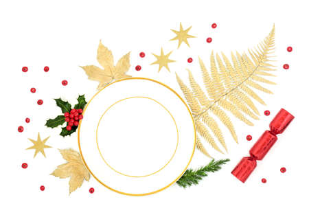 Christmas place setting abstract layout with porcelain plate, gold leaves, holly with loose berries, fir, stars and Xmas cracker on white background. Festive design for  Xmas and New Year. Top view.の写真素材