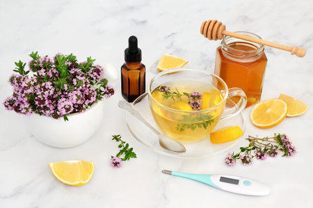 Natural medicine for flu & cold virus with thyme herb, honey & lemon in a tea cup with thermometer and essential oil bottle. Immune boosting medication, is anti bacterial, antiseptic and anti viral. On marble.の写真素材