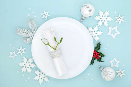 Christmas table setting with white plate, napkin, mistletoe,  bauble tree  decorations, holly and...