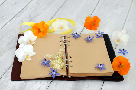 Leather bound journal or diary with blank pages for personal notes or story, with orchid flowers, nasturtium and borage herb flowers. On rustic wood background.の写真素材