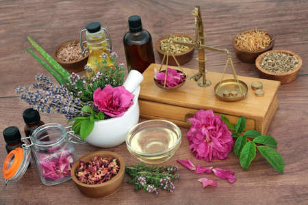 Natural remedy to treat eczema, acne and psoriasis. Preparation of herbal plant based medicine for skincare concept with old brass scales, herbs, flowers, essential oil bottles. On rustic wood.の写真素材