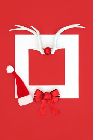 Christmas santa hat with reindeer antlers, gift bow on red background with white frame border. Traditional  festive symbols for the holiday season.の写真素材