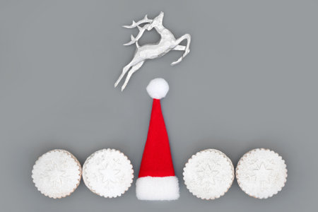Christmas holiday festive symbols with santa hat, reindeer and mince pies on gray background. Traditional tree decorations and food abstract minimal composition for Xmas and New Year season.の写真素材