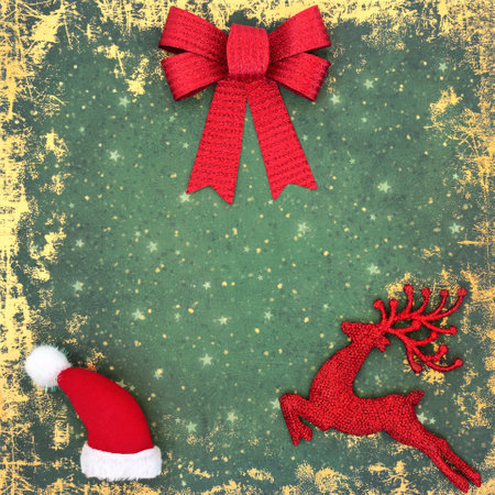 Festive Christmas background with bow, santa hat and reindeer tree bauble decorations in red on grunge green background. Traditional symbols for the Xmas holiday season.の写真素材