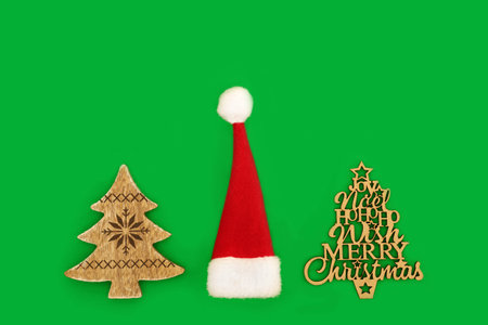 Retro rustic style Christmas tree wooden decorations with red santa hat. Eco friendly minimal design for Xmas and New Year holiday season on green background.の写真素材