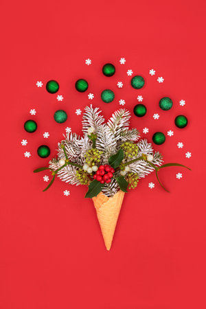 Christmas fun decorative surreal ice cream cone concept with snow covered fir, winter greenery and green tree decorations on red. Festive nature abstract fun design for Xmas holiday and New Year.の写真素材