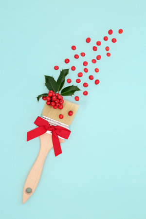 Surreal Christmas holly berry paintbrush splash concept with bow and red berries on blue background. Abstract festive design for Xmas and New Year.の写真素材