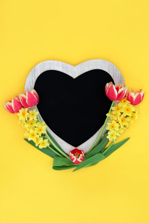 Spring flowers with heart shaped wooden chalkboard frame,  red tulip and narcissus flora on yellow background. Abstract Easter Mothers Day minimal nature floral composition with copy space.の写真素材