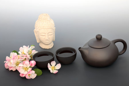 Japanese tea ceremony for inner peace, harmony and mindfulness with Buddha statue, ceramic tea set and apple blossom flowers. Healthy traditional asian culture concept on gradient grey.の写真素材