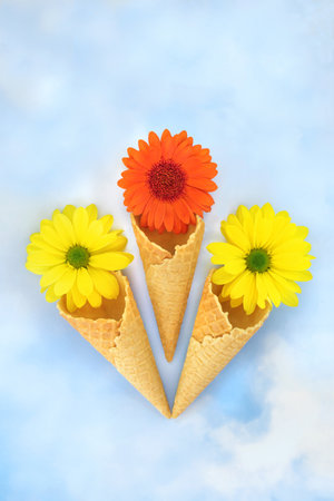 Surreal ice cream waffle cones with summer flowers on blue sky cloud background. Abstract minimal floral nature concept for the holiday season.の写真素材