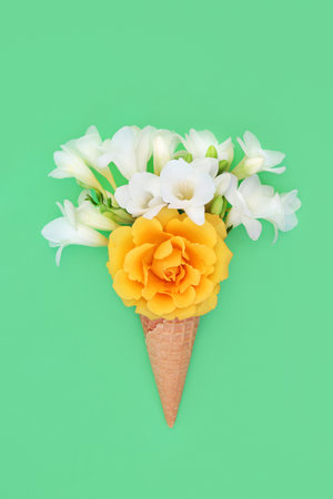 Summer surreal ice cream waffle cone with rose and freesia flowers on pastel green background. Minimal trendy beautiful nature floral surreal gift. Flat lay, copy space.の写真素材