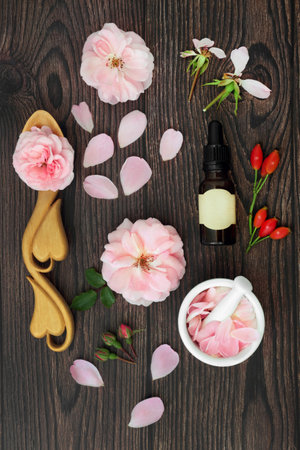 Rose flower essence with flowers for aromatherapy essential oil and rosehips for natural herbal plant medicine. Immune system boosting, high in antioxidants, anthocyanins, vitamin C. On rustic wood.の写真素材