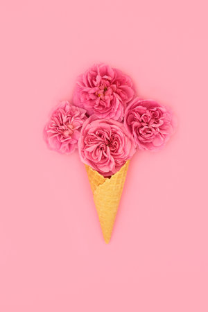 Creative surreal ice cream waffle cone with red rose flowers on pink background. Beautiful bizarre Valentines, Mothers Day, anniversary or birthday gift bouquet. Nature food concept.の写真素材