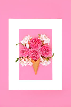 Surreal rose and freesia flower ice cream cone Composition. Creative nature food gift concept for Valentines birthday anniversary or Mothers Day. White frame on pink background.の写真素材