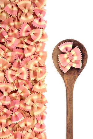 Healthy farfalle bow tie Italian pasta with olive wood spoon on white background. Beetroot food dye used for pink colour. Healthy gourmet Mediterranean cooking eating concept. Flat lay top view.の写真素材