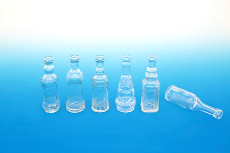 Theres always one abstract concept with line of old glass retro bottles with one fallen over. On gradient blue white background.の写真素材