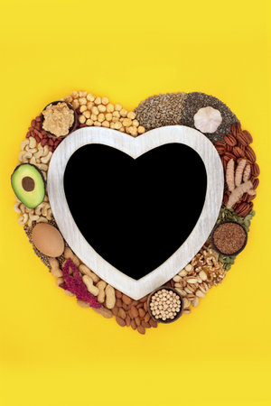 Health food high in lipds. Ingredients with unsaturated fats for healthy heart and low cholesterol levels with nuts, seeds, vegetables, dairy and grain. Chalk board blackboard wreath on yellow.の写真素材