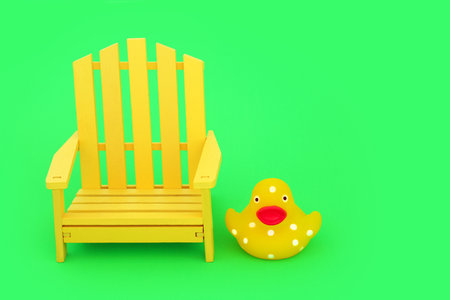 Crazy surreal minimal composition with wooden slatted yellow chair and spotted squeaky duckling on vivid green background. Fun contrast concept. Copy space.の写真素材