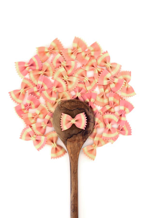 Italian bow tie farfalle Italian pasta food with olive wood spoon on white background. Beetroot food dye used for pink color. Healthy gourmet eating concept. Flat lay.の写真素材