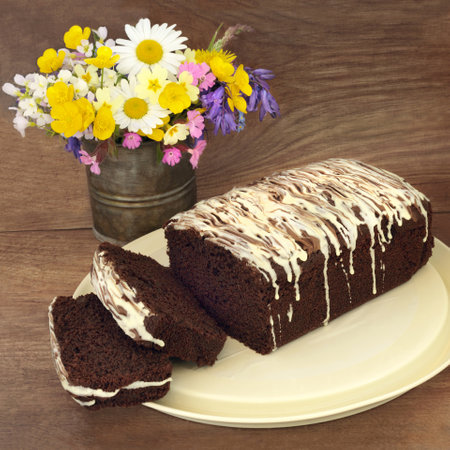 Homemade chocolate chip cake with icing drizzle on metal tray on rustic wood background with Spring  wildflower arrangement. Sweet dessert food for afternoon tea.の写真素材