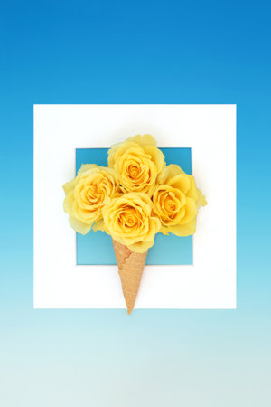 Surreal ice cream cone with yellow rose flowers on gradient blue background and white square frame. Edible fun summer nature bouquet abstract design.の写真素材