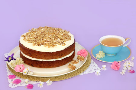 Carrot and walnut cake for afternoon tea with teacup and summer flowers on purple background. Homemade delicious food concept for birthday party or Mothers Day.の写真素材