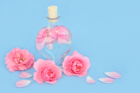Rosewater for natural skincare in heart shaped bottle with pink rose flowers and petals on blue. Can balance ph of skin oils, reduce redness, naturally hydrates skin.の写真素材