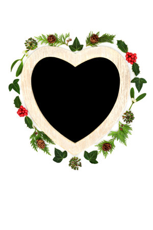 Christmas heart shape wreath with holly, mistletoe traditional winter greenery. Romantic symbol for the festive holiday season on white background with chalkboard.の写真素材
