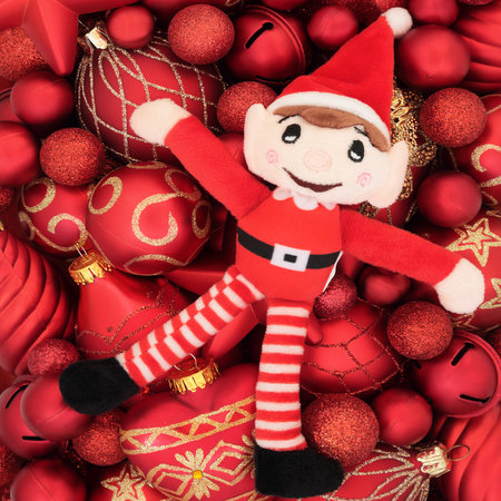 Christmas Eve elf toy with red gold bauble ornaments abstract background. Festive symbols Merry...