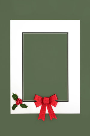 Christmas holly berry and red bow background with white frame on green. Minimal abstract festive design for greeting card, label, invitation, menu, gift tag.の写真素材
