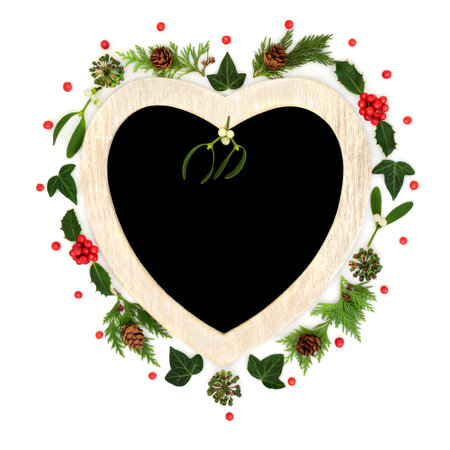 Christmas heart shape wreath with holly, berries, mistletoe, ivy and fir. Traditional romantic symbol for the festive holiday season on white background with chalkboard.の写真素材