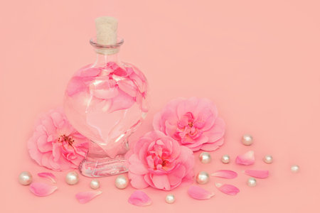 Rose flower perfume in heart shaped bottle with pearls, flowers and loose petals on pink. Natural beauty product, gift for Valentines Day, birthday, anniversary or Mothers day.の写真素材