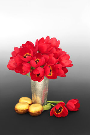Gold Easter eggs and red tulip flowers in a vase on gradient gray black white background. Spring floral, festive  luxury treats for the holiday season.の写真素材