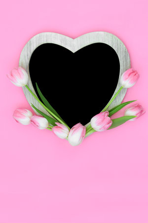 Heart shape pink tulip flower frame with chalkboard on pink background.. Minimal floral Spring, Mothers Day, Anniversary, birthday and Easter nature design.の写真素材
